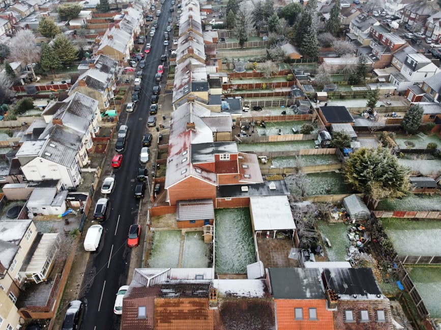 Aerial view of residential gardens and houses along Mile End Road in Stepney during winter, showing fenced backyards filled with various garden features and maintenance activities. Several gardens hav