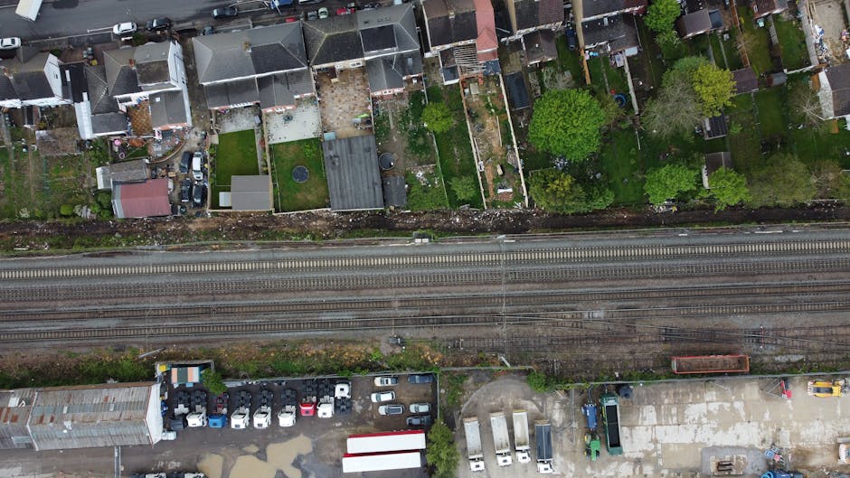 Aerial view of residential gardens and houses along Mile End Road in Stepney during winter, showing fenced backyards filled with various garden features and maintenance activities. Several gardens hav